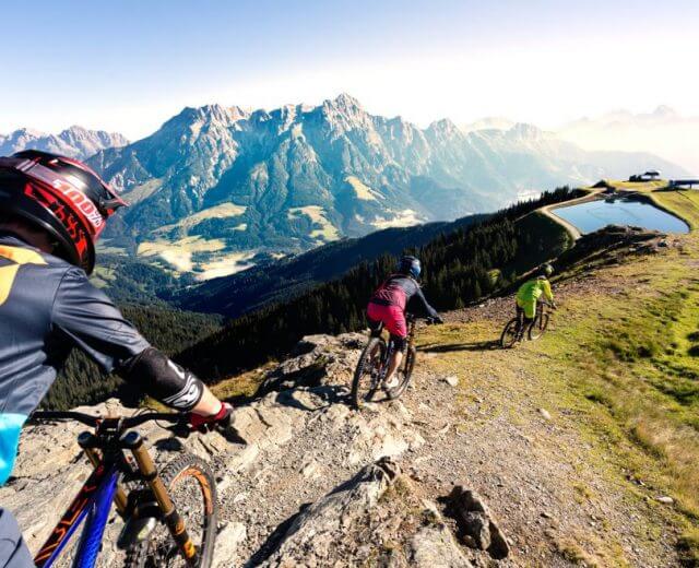 Trzech rowerzystów górskich zjeżdża skalistym szlakiem w Lato w Saalbach Hinterglemm Leogang Fieberbrunn.
