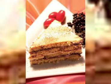 Kawałek warstwowego tiramisu z owocami czarnego bzu na talerzu z pomidorkami koktajlowymi i jagodami.