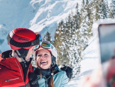 Para w sprzęcie narciarskim uśmiecha się do zdjęcia na ośnieżonej górze Ski amadé z drzewami w tle.