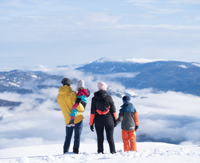 Familie ┬®Salzburger Lungau Rodzice z dwójką dzieci patrzą na osnute chmurami i ośnieżone szczyty gór Salzburskiego Lungau.