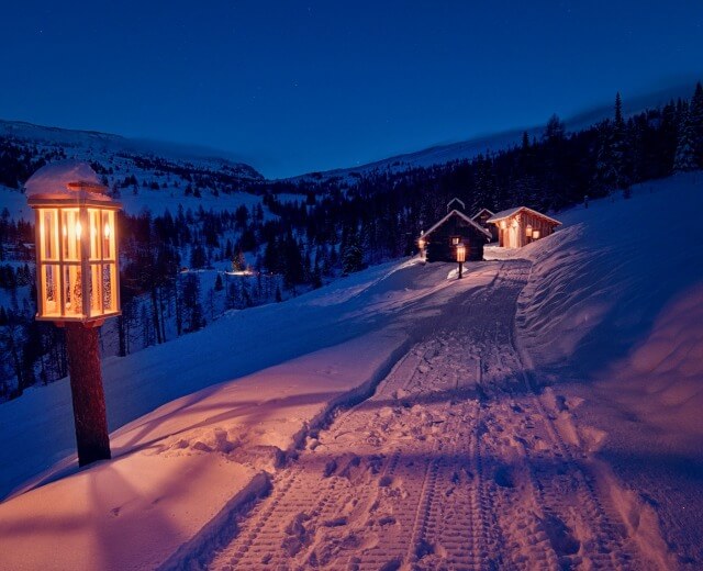 Ośnieżona ścieżka z latarnią prowadzi do przytulnego domku, przywodząc na myśl Adwent w Salzburskim Lungau o zmierzchu.