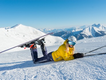 Narciarz w żółtej kurtce uśmiecha się na śniegu, ciesząc się zabawą w Raurisertal z górami w tle.