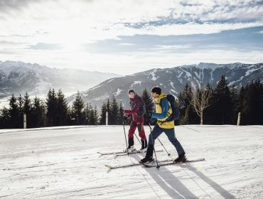 skitour-zum-ronachkopf—ski-tour-ronachkopf-c-zell-am-see-kaprun-tourismus Dwie osoby jeżdżą na nartach na ośnieżonym stoku górskim podczas Skitury w Zell am See-Kaprun pod częściowo zachmurzonym niebem.
