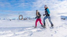 Dwie kobiety na rakietach śnieżnych w górach, cieszące się zimowymi wędrówkami w Wildkogel-Arena pod słonecznym niebem.