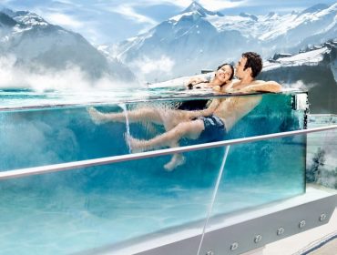 tauern_spa_tsk_keyvisual_winter_paerchen_ausschnitt_web-1170×658 Para relaksuje się w basenie bez krawędzi na dachu, mając za sobą ośnieżone góry Zima w Tauern SPA Zell am See-Kaprun.