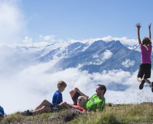 Rodzina cieszy się piknikiem w górach; dwoje dzieci bawi się, a chmury i ośnieżone szczyty wypełniają tło.