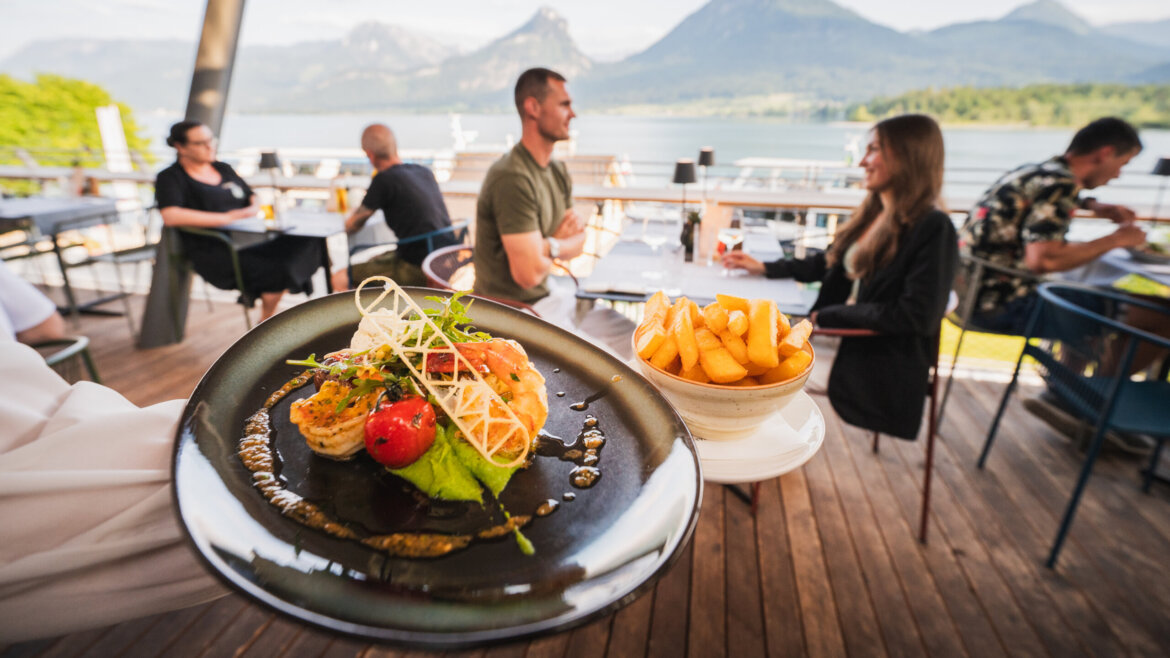 Wykwintny posiłek z frytkami serwowany jest na świeżym powietrzu, z widokiem na jezioro i kolej zębatą na górę Schafberg. (Powiększony widok)
