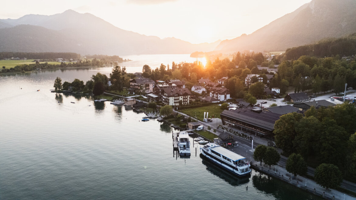 Wioska nad jeziorem o zachodzie słońca w Salzburgu Salzkammergut, z zacumowanymi łodziami i górami w tle.