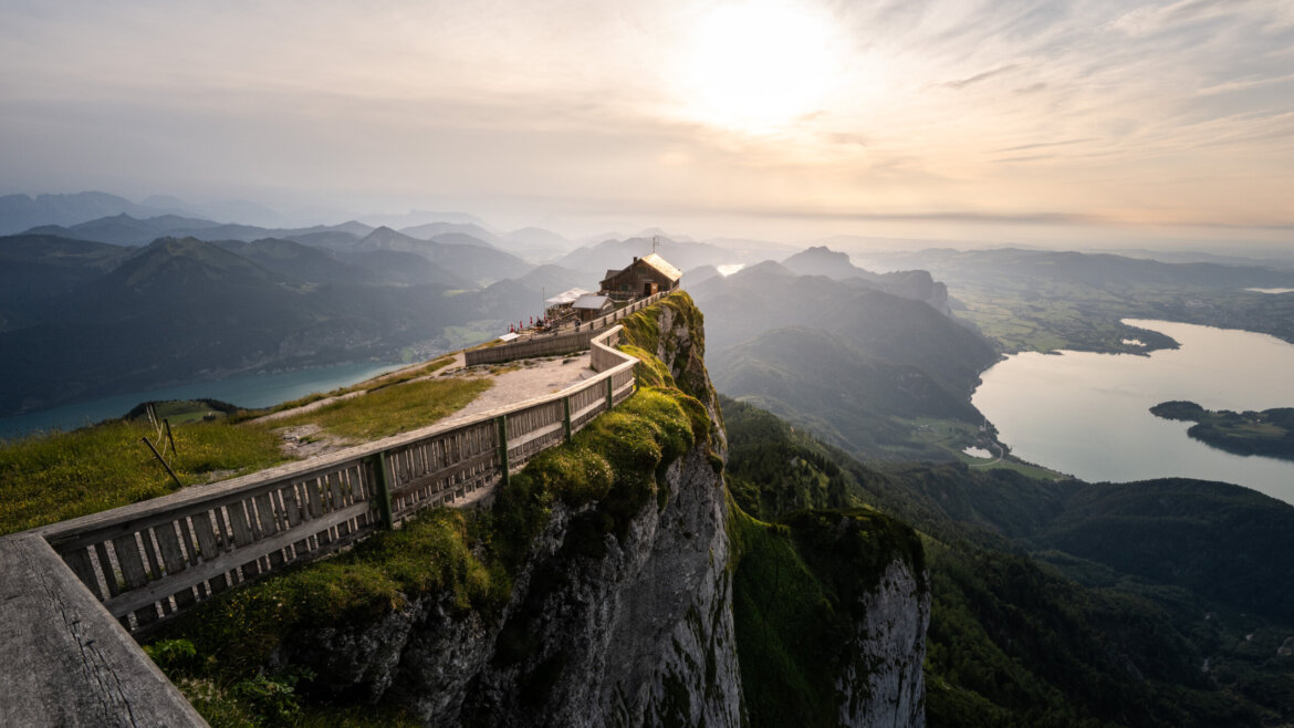 Górska ścieżka z drewnianym płotem prowadzi do schroniska w pobliżu kolejki zębatej na górę Schafberg o zachodzie słońca. (Powiększony widok)