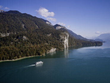 DJI_0544 Łódź płynie po jeziorze Wolfgangsee, otoczona zalesionymi górami pod czystym, błękitnym niebem. Rejsy statkiem.