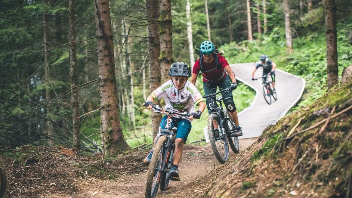 Trójka kolarzy na rowerach górskich - chłopiec, mama i ojciec - zjeżdża w szlakiem Flow One w regionie Hochkönig na Ziemi Salzburskiej. Na ich twarzach napięcie.