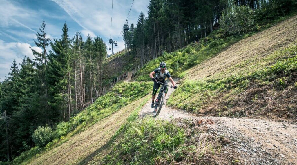 Osobisty zjazd na rowerze górskim po krętym, polnym szlaku przez zalesione wzgórze pod błękitnym niebem.