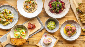 Kräutergerichte_Hochkönig Różnorodne dania dla smakoszy, idealne na turystkę zielarską, ułożone na rustykalnym drewnianym stole.