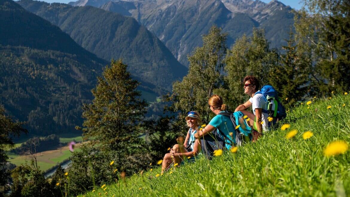Trójka turystów odpoczywa na szlaku panoramicznym w Wysokich Taurach, napawając się górskimi widokami.