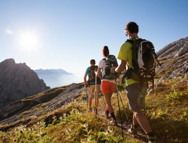 Trójka wędrowców z kijkami węDrownymi i plecakami o wschodzi słońca na szlaku pieszym w paśmie Leoganger Steinberge