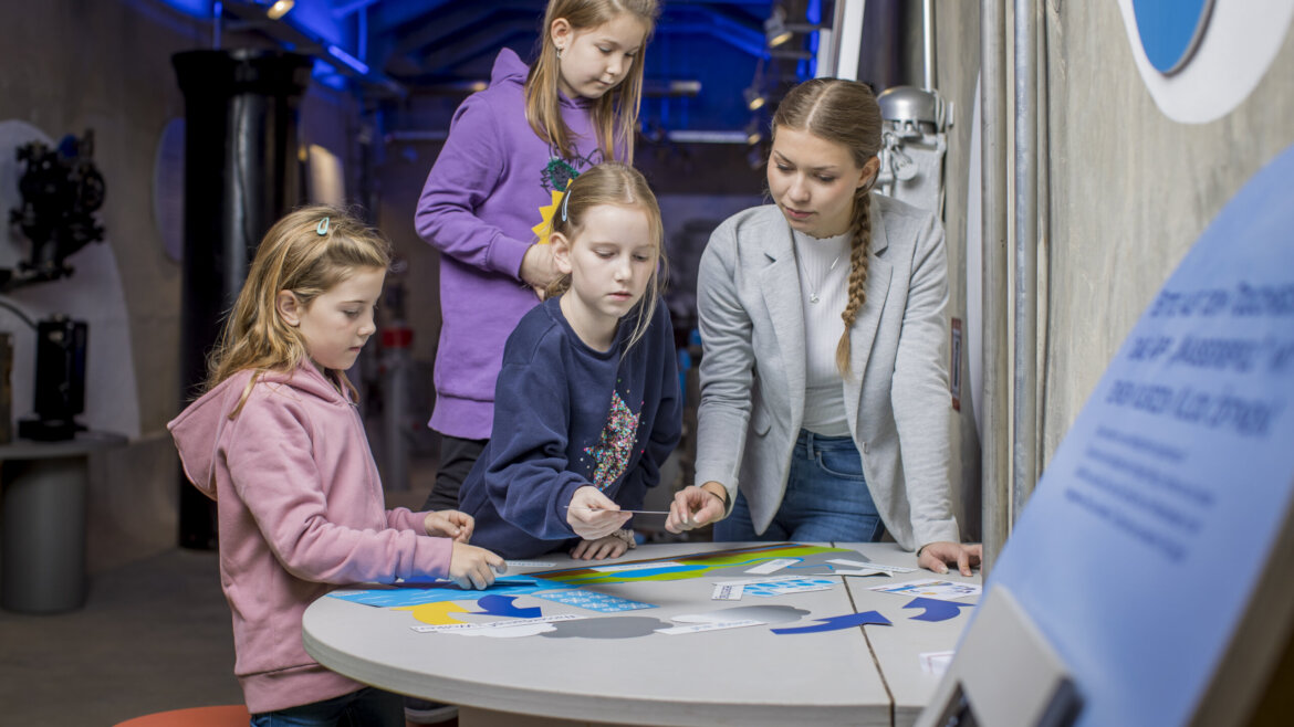 Kobieta i trzy dziewczynki układają puzzle na wystawie Salzburg Salzkammergut. (Powiększony widok)