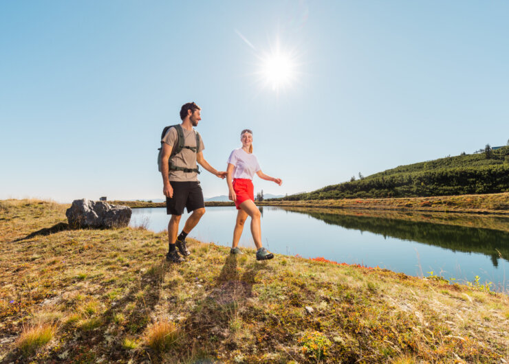 Mężczyzna i kobieta wędrują w słoneczny dzień obok spokojnego jeziora Być.Sobą latem w Lungau.