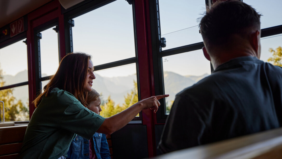 Kobieta wskazuje przez okno pociągu na kolej zębatą na górę Schafberg, góry w tle. (Powiększony widok)