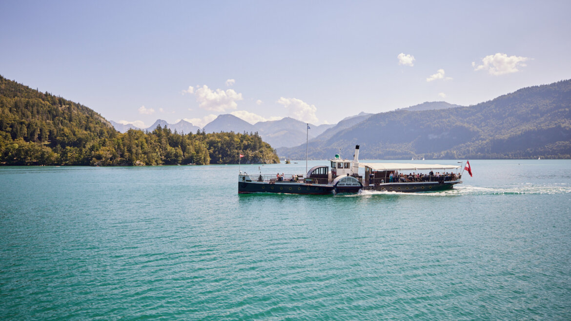 Rejs łodzią po malowniczym jeziorze Salzburg Salzkammergut otoczonym zalesionymi wzgórzami i górami pod czystym niebem.