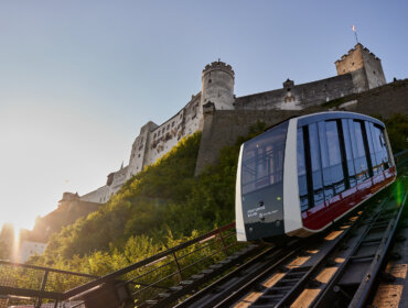 SBG_AG_230822_0046 Nowoczesna kolejka linowa, znana jako kolejka do twierdzy, wspina się stromą ścieżką do zamku na wzgórzu o zachodzie słońca.