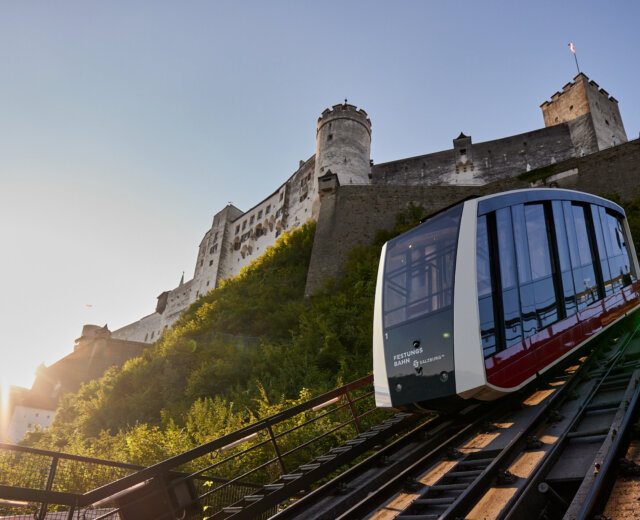 Nowoczesna kolejka linowa, znana jako kolejka do twierdzy, wspina się stromą ścieżką do zamku na wzgórzu o zachodzie słońca.