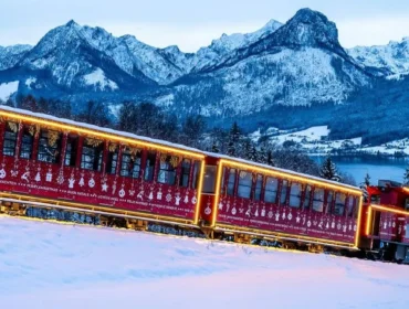 Czerwony pociąg udekorowany światłami jedzie przez zaśnieżone góry Salzburga Salzkammergut i sosny o zmierzchu.