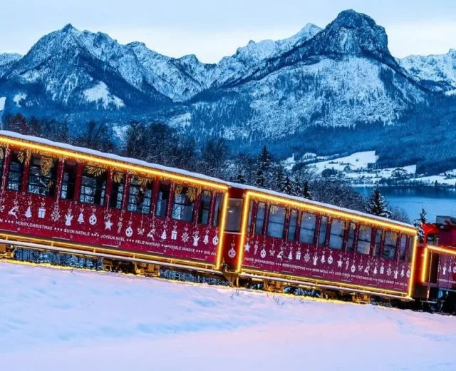 Czerwony pociąg udekorowany światłami jedzie przez zaśnieżone góry Salzburga Salzkammergut i sosny o zmierzchu.