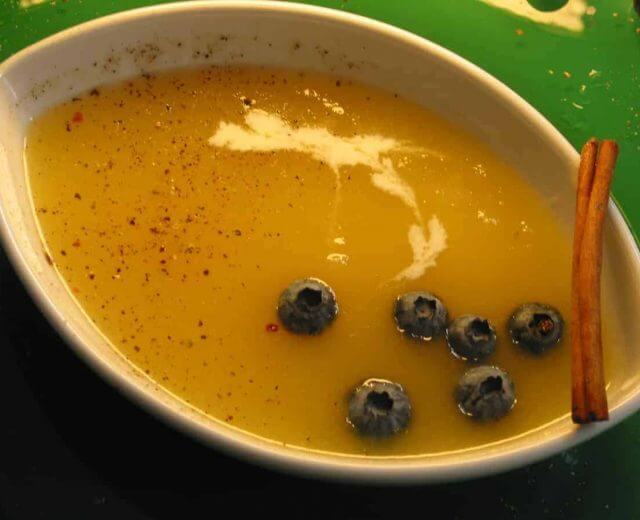 Kaltes-ApfelsxFCppchen-mit-Pfeffer-und-Heidelbeeren Zupa krem z jabłek na zimno, podana w ceramicznej miseczce w kształcie łódeczki, przybrana grubo zmielonym kolorowym pieprzem, owocami jagód i laską cynamonu.