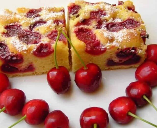Dwa kawałki smakowitego, puszystego placka z czereśniami udekorowane świeżymi, dorodnymi owocami czereśni.