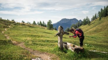 Turystka piesza z plecakiem wędrownym odpoczywa i pije wodę z górskiej drewnianej studzienki na Postalm