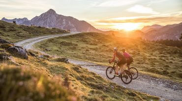 Dwóch kolarzy na rowerach górskich przemierza szlak przez Postalm w promieniach zachodzącego słońca.