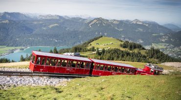 Pchane przez lokomotywę czerwone wagoniki kolejki zębatej jadą w kierunku stacji górnej tuż pod szczytem góry Schafberg.