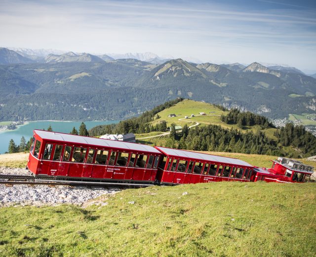 Pchane przez lokomotywę czerwone wagoniki kolejki zębatej jadą w kierunku stacji górnej tuż pod szczytem góry Schafberg.