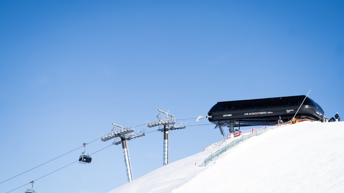 Kolejka Aussichtsbergbahn w Dachstein West © Dachstein Tourismus AG, Chris Eder Media Stacja wyciągów narciarskich w Aussichtsbergu z wyciągami krzesełkowymi wjeżdżającymi na ośnieżoną górę w regionie Dachstein West. (Powiększony widok)