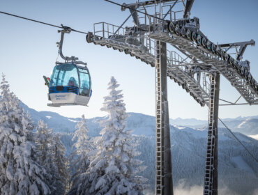 Gondola narciarska szybuje ponad ośnieżonymi drzewami i górami - prawdziwa magia Zima w Dachstein West pod czystym, błękitnym niebem.