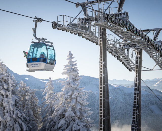 Donnerkogelbahn Winter © Dachtein Tourismus AG, MirjaGeh Gondola narciarska szybuje ponad ośnieżonymi drzewami i górami - prawdziwa magia Zima w Dachstein West pod czystym, błękitnym niebem.