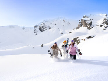Trzy osoby w zimowych ubraniach idą przez głęboki śnieg - Jesteśmy pokoleniem zimy - niosąc deski snowboardowe.