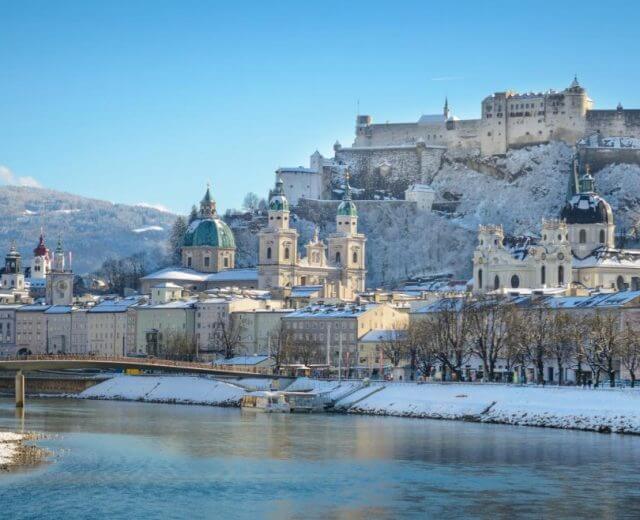 Widok salzburskiego Starego Miasta w zimowej, śnieżnej szacie, z twierdzą Hohensalzburg, katedrą i kościołem Uniwersyteckim.