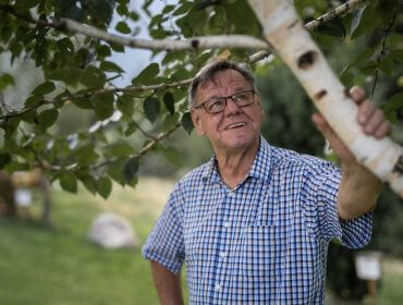 Starszy mężczyzna w okularach i koszuli w kratę, uśmiechnięty, delektujący się magią kręgu drzew na trawiastym trawniku.