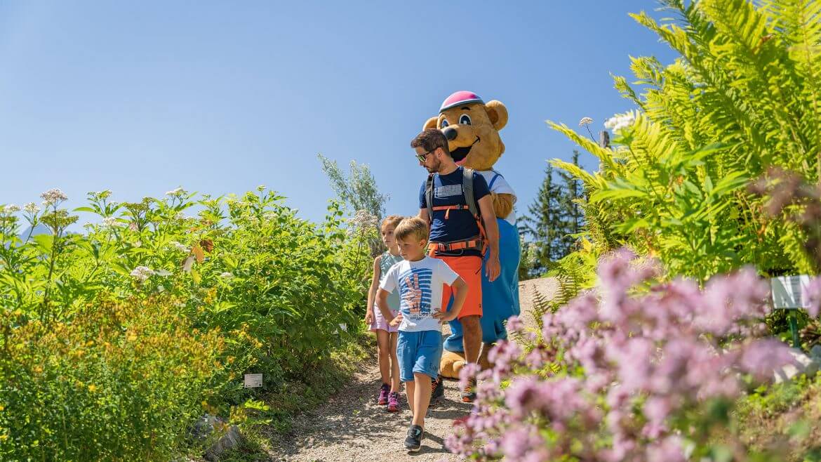 Niedźwiadek Bruno towarzyszy rodzinie z dziećmi przez alpejski ogród w swoim parku rozrywki i rekreacji na Hornspitz w Russbach.
