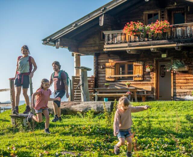 Rodzina z dwójką dzieci cieszy się słonecznym dniem przed drewnianym domkiem na wsi.