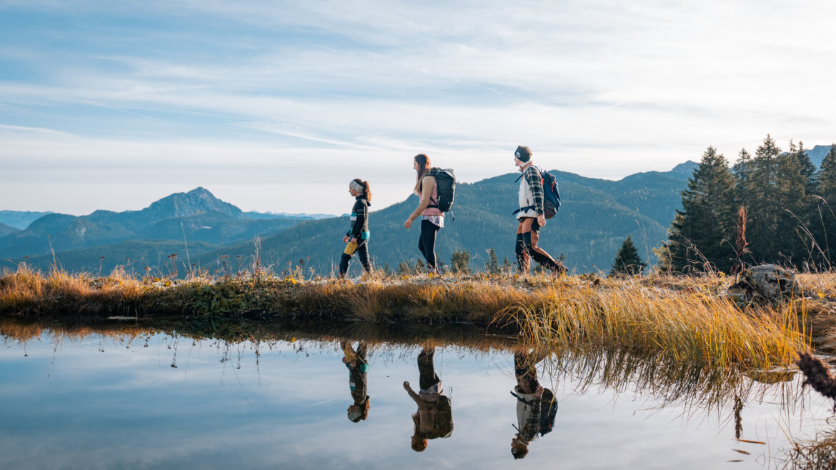 Trzech wędrowców spaceruje nad górskim jeziorem w Dachstein West, odbijając turystykę pieszą wśród lasów i gór.