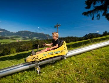 Chłopiec w żółtych saneczka zjeżdża w dół po letnim torze saneczkowym na Karkogel w Abtenau.