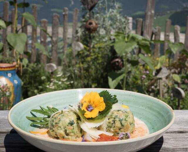 Apetycznie podane knedle bułczane przystrojone ziołami i kwiatami jadalnymi, w tle wiejski ogródek ziołowy.