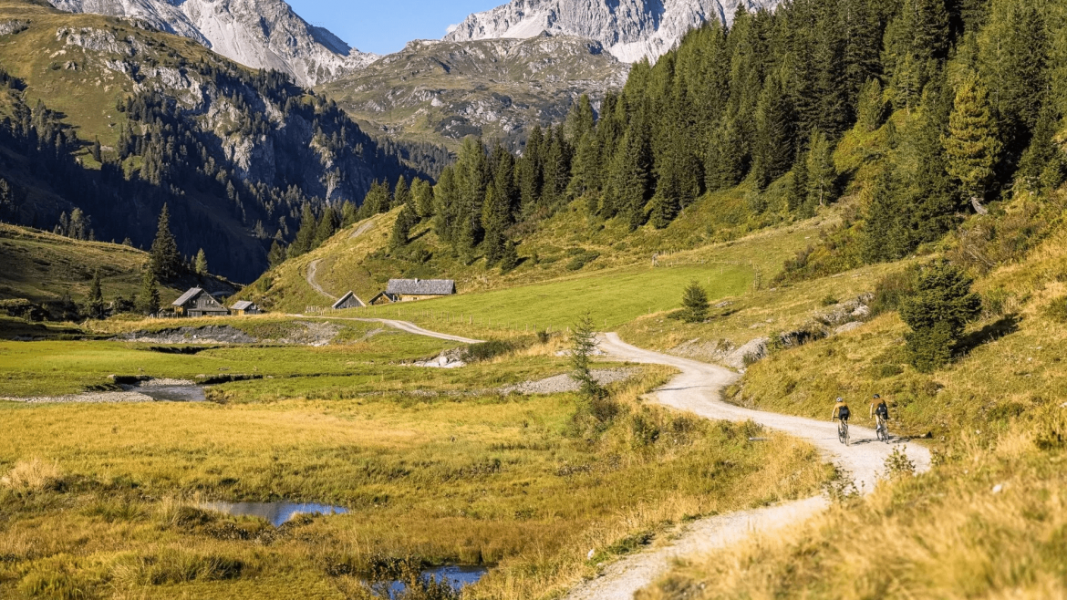 Dwójka kolarzy górskich przemierza górskie ścieżki rowerowe pośród alpejskich łąk i sklanych górskich ścian.