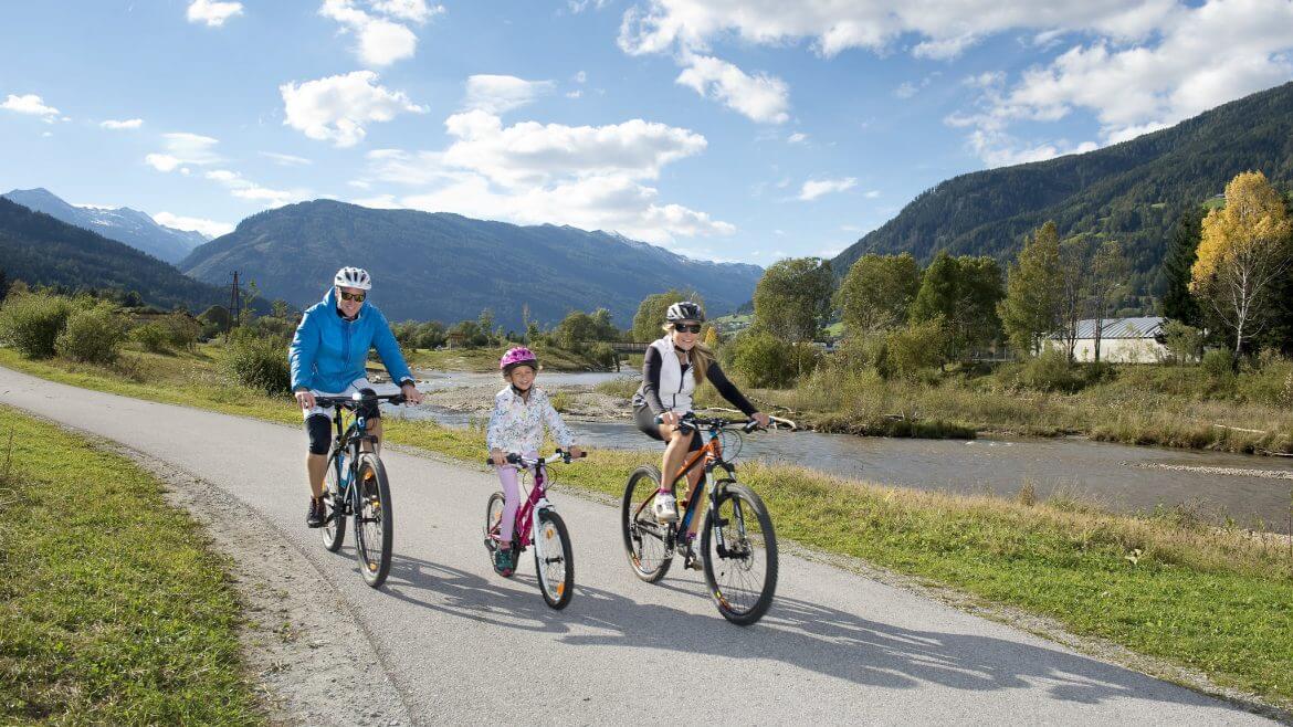 Rodzice z córeczką przemierzają zrelaksowani najpiękniejszą w Austrii trasę rowerową nad rzeką, wzdłuż rzeki Mury.