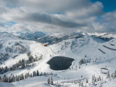 Małe jezioro, ośnieżone szczyty i sosny - idealne na narty przyjazne dla środowiska pod pochmurnym, błękitnym niebem.