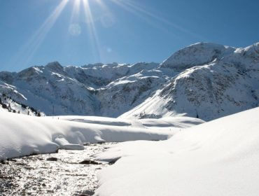 Pokryte śniegiem góry w jasnym słońcu, idealne na zrównoważony rozwój narty wzdłuż śnieżnego strumienia w dolinie.