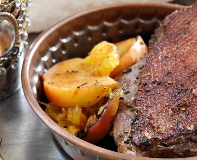 Gotowana pierś z kaczki z prażonymi jabłkami i pomarańczami, inspirowana pieczoną gęsią, podawana w brązowej miseczce.