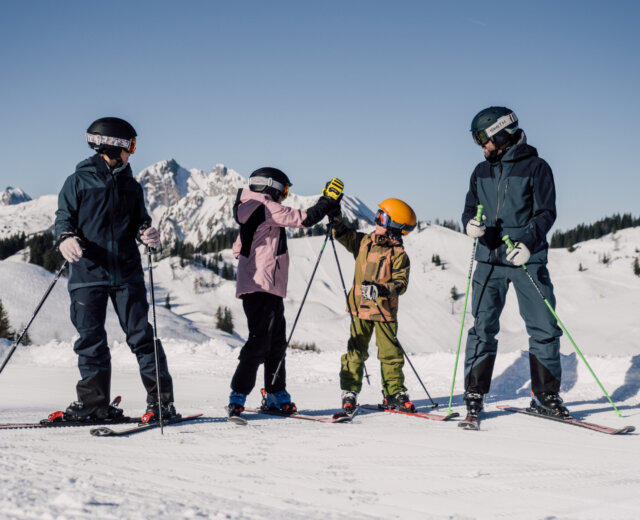 Cztery osoby w sprzęcie narciarskim cieszą się ferie z rodziną St. Johann na ośnieżonym stoku z widokiem na góry.